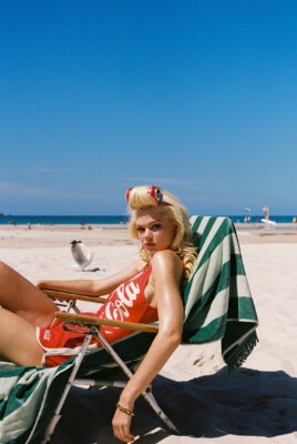model ayla sitting on tan chair with coca cola can in hair on beach