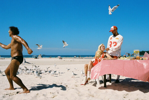 models ayla and bruno at table and guy of speedos running on beach