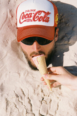 model bruno burried in sand wearing coca cola x something very special hat